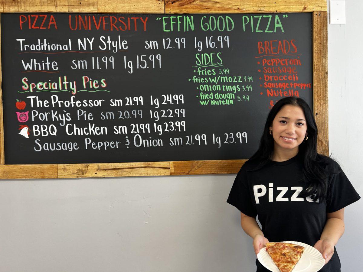 Pizza University employee Simone Borzilo poses with a fresh slice next to the menu. - Staff Writer / Isaac Linsk