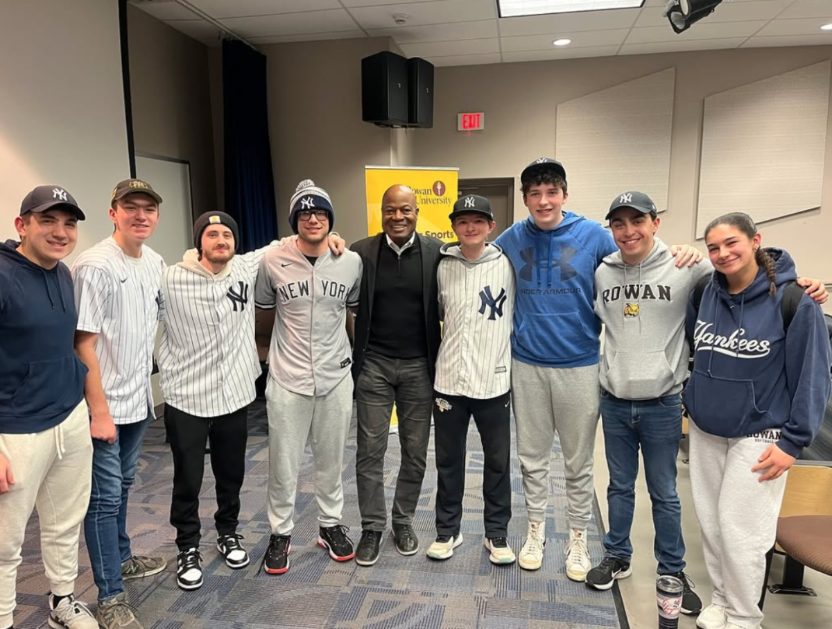 Students pose with Dave Sims for a photo in their Yankees gear. - Photo via @rowansportscam on Instagram. 