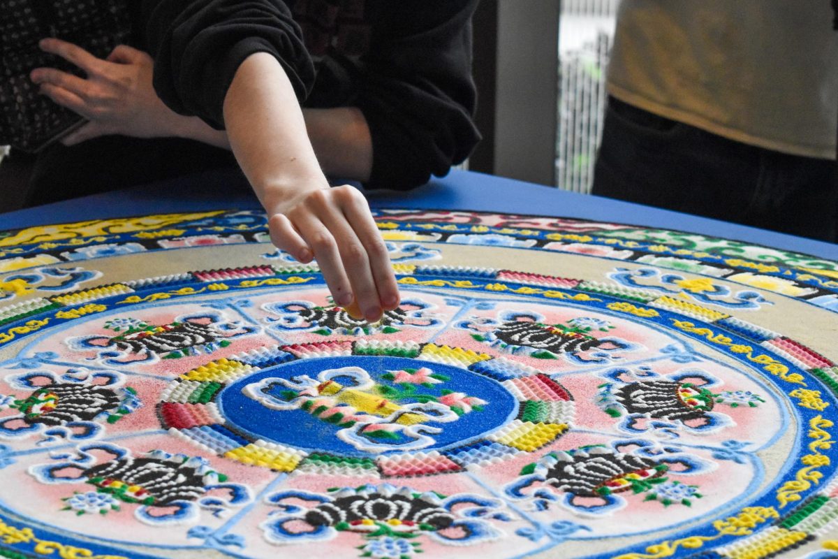 An event attendant scatters the sands from the sand mandala as part of its ritual destruction at Discovery Hall on Rowan's Campus. Glassboro, NJ. Thursday, April 10, 2025. - Staff Photographer / Owen Miller