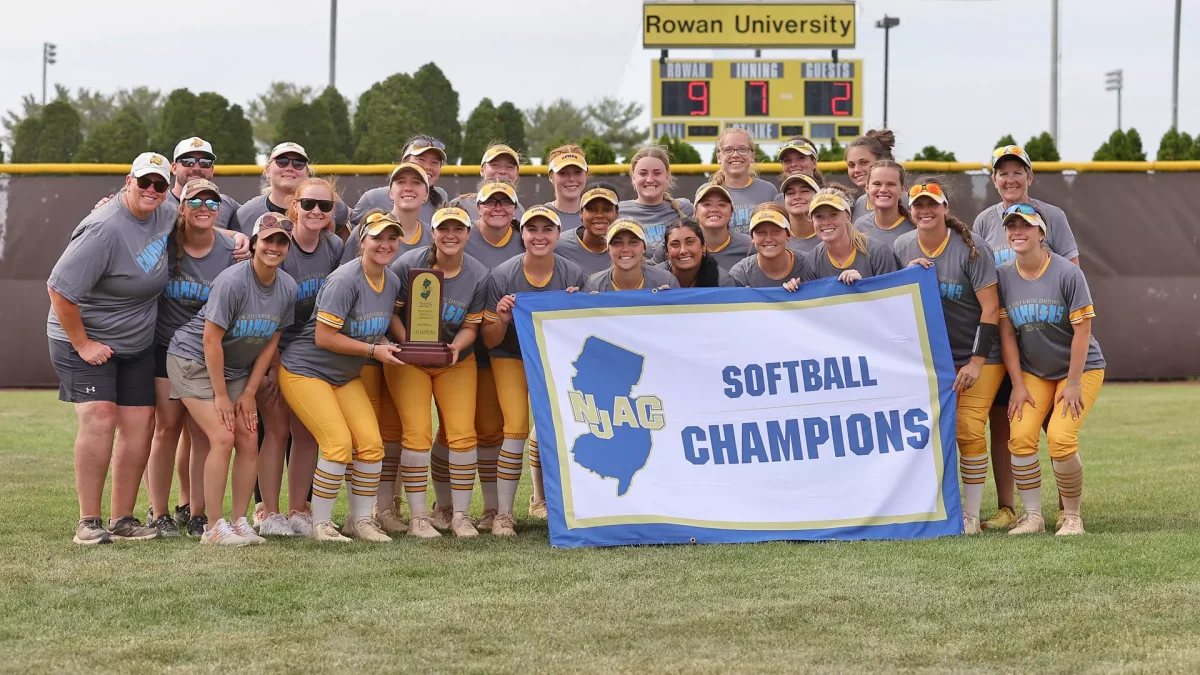 The Rowan softball team poses with their NJAC Champions banner. The program has won back-to-back conference titles for the first time since 2001. - Photo via Rowan Athletics
