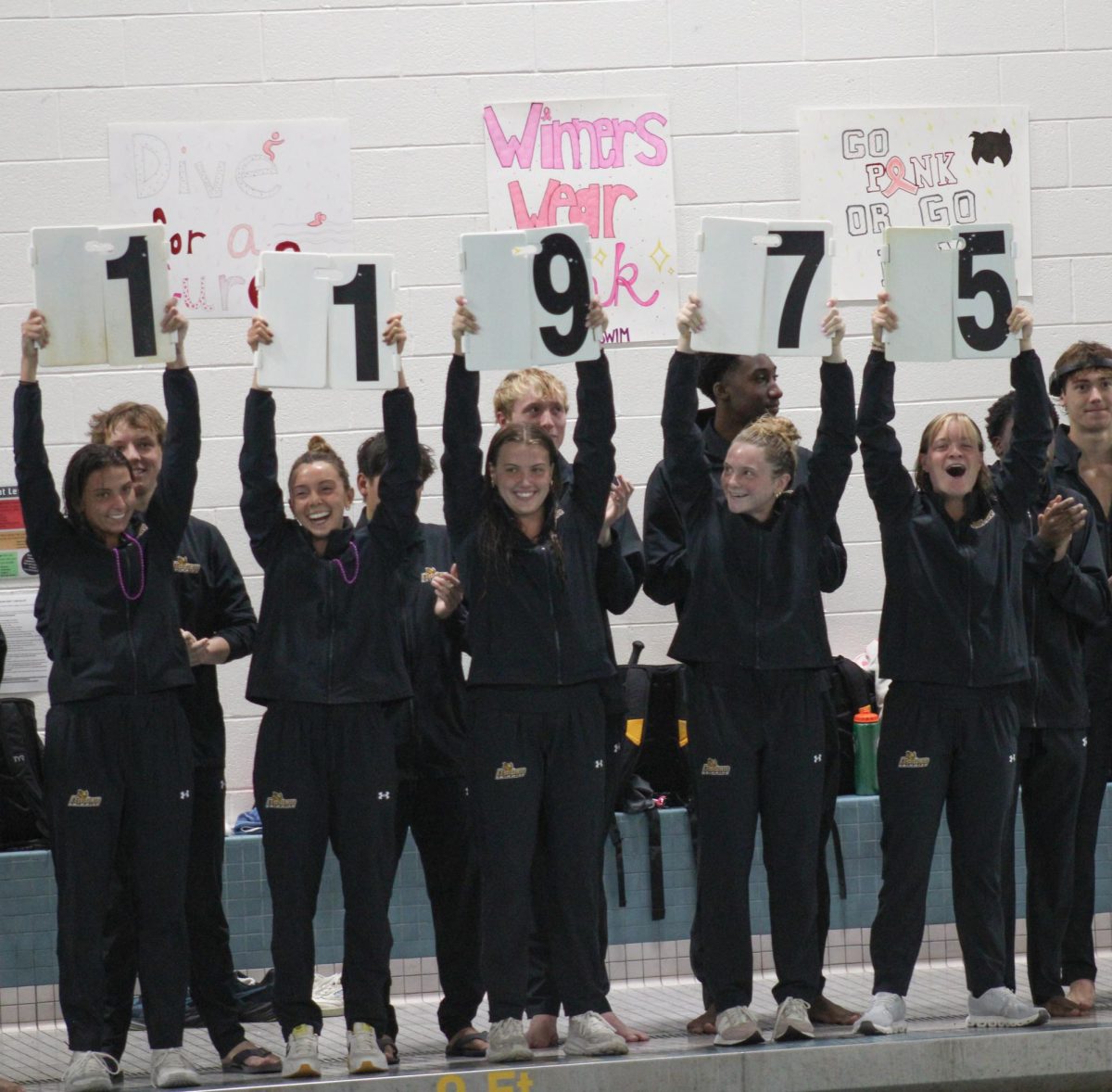 Members of the Rowan women’s swimming team hold up signs displaying the total amount of funds raised prior to their season-opening meet against the Stevens Institute of Technology. Glassboro, N.J. Saturday, Oct. 11, 2025. (Contributor / Melanie Barahona)